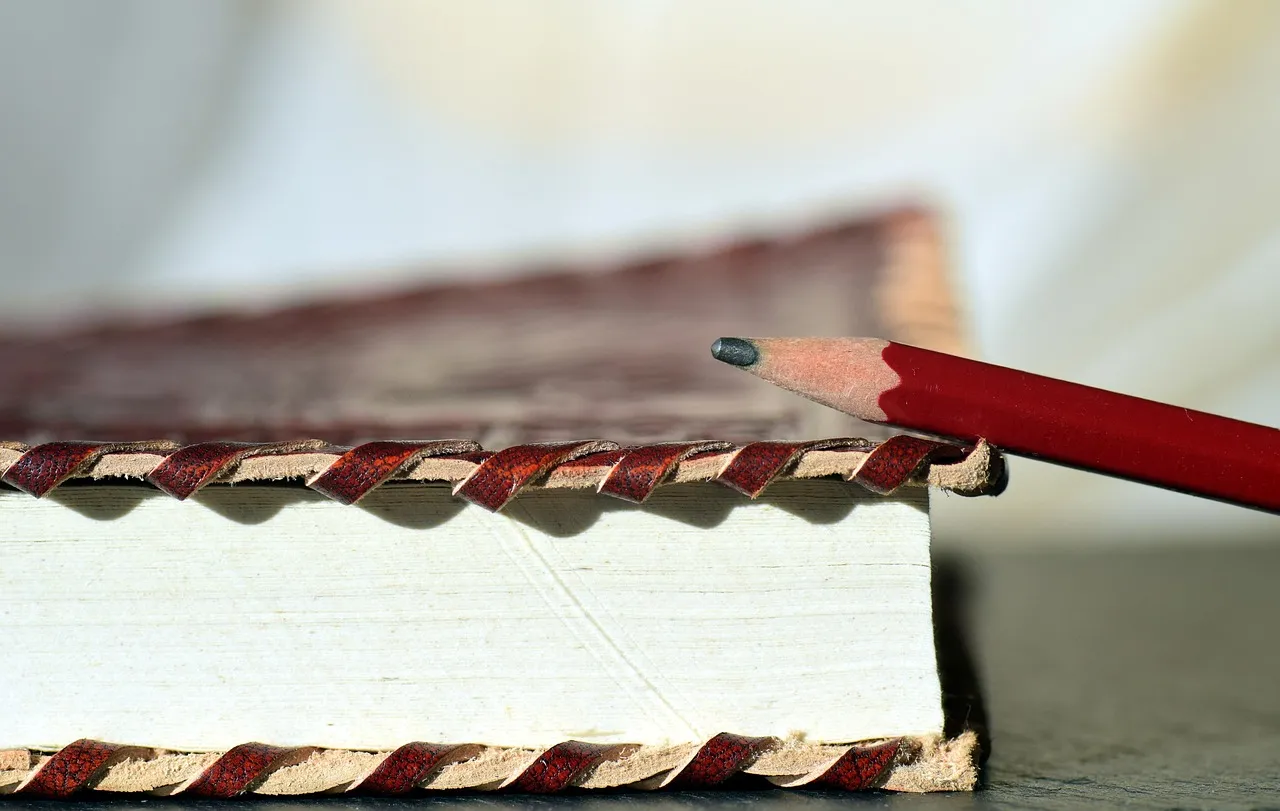 Close-up of a book's stitched headband next to a red pencil